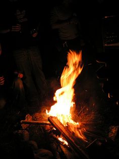 people are gathered around a campfire in the dark, with bright flames coming from it