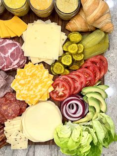 an assortment of cheeses, meats and vegetables on a cutting board with jars of mustard