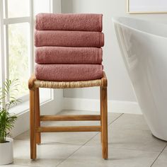 a stack of towels sitting on top of a wooden stool next to a bath tub