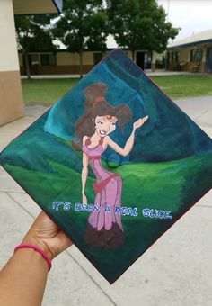 a hand holding up a graduation cap with an image of a woman in a pink dress