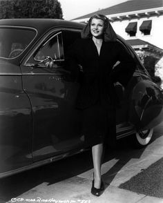 an old photo of a woman standing next to a car