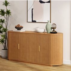 a wooden cabinet with two bowls on top and a plant in the corner next to it