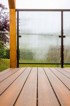 an empty wooden deck with rain falling on the glass door and grass in the background