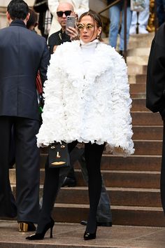 a woman is walking down the steps wearing a white dress and feathered jacket with black heels