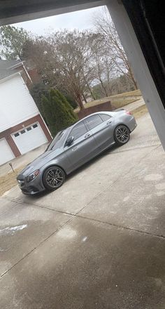 a silver car parked in front of a house on a driveway next to a garage