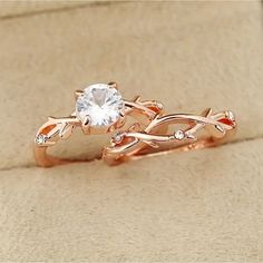 a rose gold ring with a white topazte stone in the center and leaves on each band