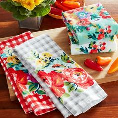 three colorful kitchen towels sitting on top of a cutting board