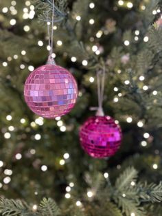 two pink disco ball ornaments hanging from a christmas tree with white lights in the background