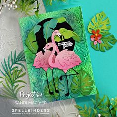 two pink flamingos standing next to each other on top of green leafy paper