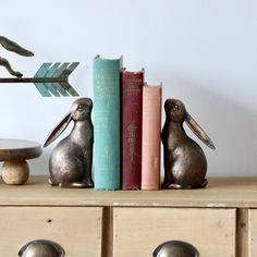 two metal rabbits sitting on top of a wooden dresser next to books and an arrow