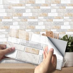 a person is holding a white keyboard in front of a brick wall and potted plant