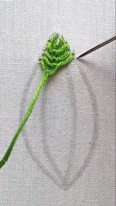 a green flower is being worked on by someone using scissors and thread to make it