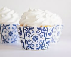 three cupcakes with white frosting in blue and white paper cups on a table