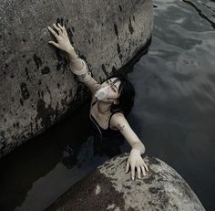 a woman with her arm around a rock in the water, reaching up into the air