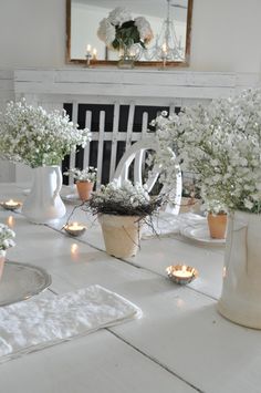 the table is set with white flowers and candles in vases on top of it