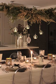 a dining room table is set with candles and christmas ornaments hanging from the chandelier