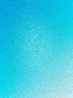 an airplane is flying in the sky above the blue water and sand below it are two surfers