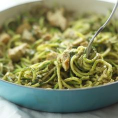 a blue pan filled with pasta and broccoli covered in pesto sauce on top of a table