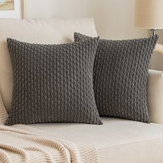 two gray pillows sitting on top of a white couch