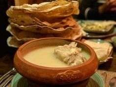 a bowl filled with soup sitting on top of a table next to tortillas