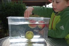 a little boy that is sitting at a table with some fruit in a container on it