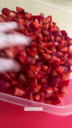 someone is picking up strawberries from a plastic container on a table with a pink surface