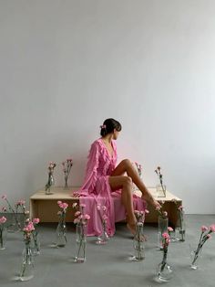 a woman in a pink dress sitting on a bench surrounded by vases and flowers