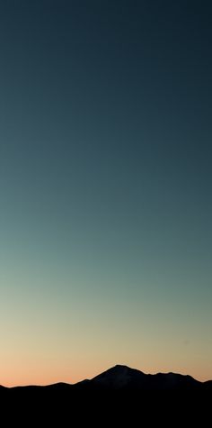 the silhouette of two people standing on top of a hill at sunset, with mountains in the background