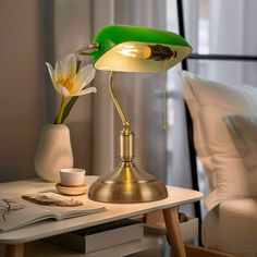 a green table lamp sitting on top of a wooden table next to a white bed