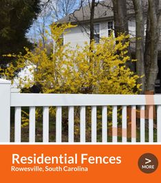 a white picket fence in front of a house with yellow flowers on the bushes and trees