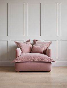 a pink chair sitting in front of a wall with white paneling and wooden floors