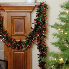 a decorated christmas tree next to a fireplace with a lit candle on it and a wreath hanging from the mantle