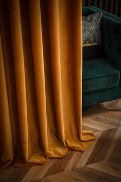 an orange curtain is open in front of a green velvet couch and wooden flooring