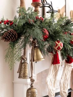 christmas decorations hanging from the mantle with bells and pine cones on it's garland