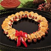 a wreath made out of pigs in a blanket on top of a black plate with red ribbon