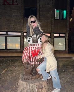 two women standing next to each other near a fake horse in front of a building