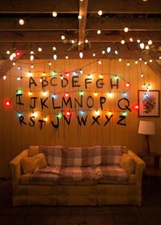 a couch sitting in front of a wooden wall covered in christmas lights and letters on it