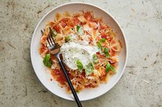 a white plate topped with pasta covered in sauce and cheese next to two black utensils