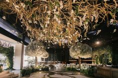 an indoor wedding venue with white flowers and greenery hanging from the ceiling, surrounded by chandeliers