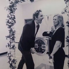 a man and woman standing next to each other in front of a clock with vines on it