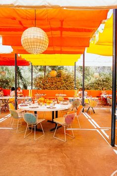 an outdoor dining area with orange and yellow umbrellas over tables, chairs and lamps