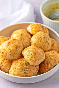 a white bowl filled with cheesy biscuits next to a small bowl of dipping sauce