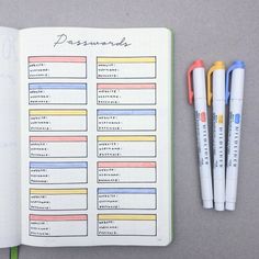 an open planner with pens and markers next to it on a gray surface, surrounded by two notebooks