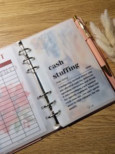 an open planner sitting on top of a wooden table next to a pen and feather