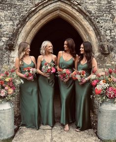 bridesmaids in green dresses standing outside an old stone building with their bouquets