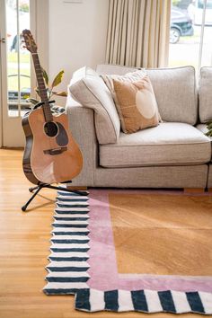 a guitar sitting on top of a wooden floor next to a white couch and window