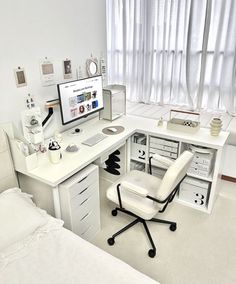 a white desk with a computer on top of it next to a bed and window