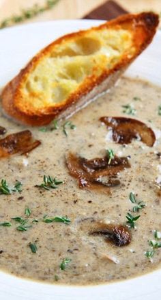 a white bowl filled with mushroom soup on top of a wooden table next to a piece of bread