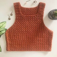 an orange crocheted top next to earrings and a plant