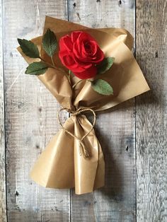 a red rose wrapped in brown paper on top of a wooden table with twine